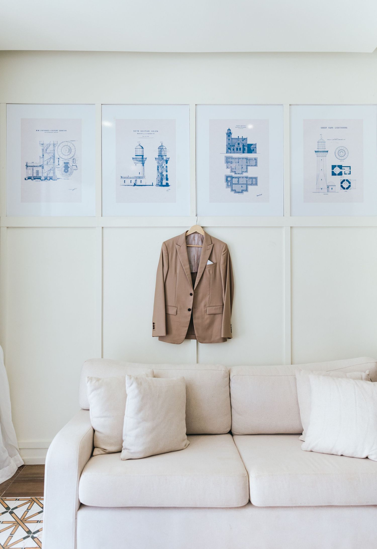 Minimalist white room with architectural drawings on wall and tan blazer displayed.
