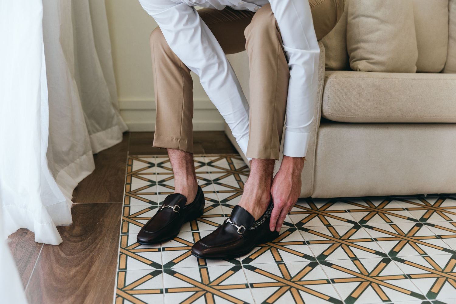 Person in formal attire adjusting shoes on patterned floor.