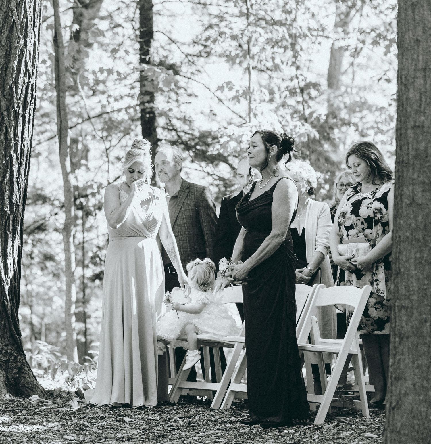 Black and white photo of wedding guests seated outdoors among trees.