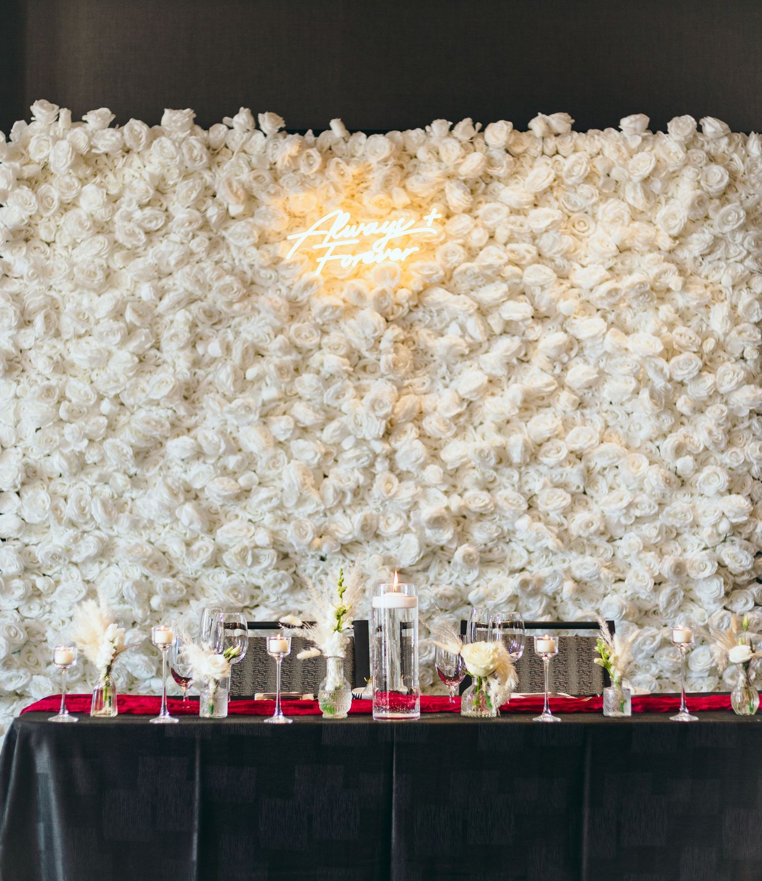 Elegant wedding reception table with white floral wall backdrop and black tablecloths.