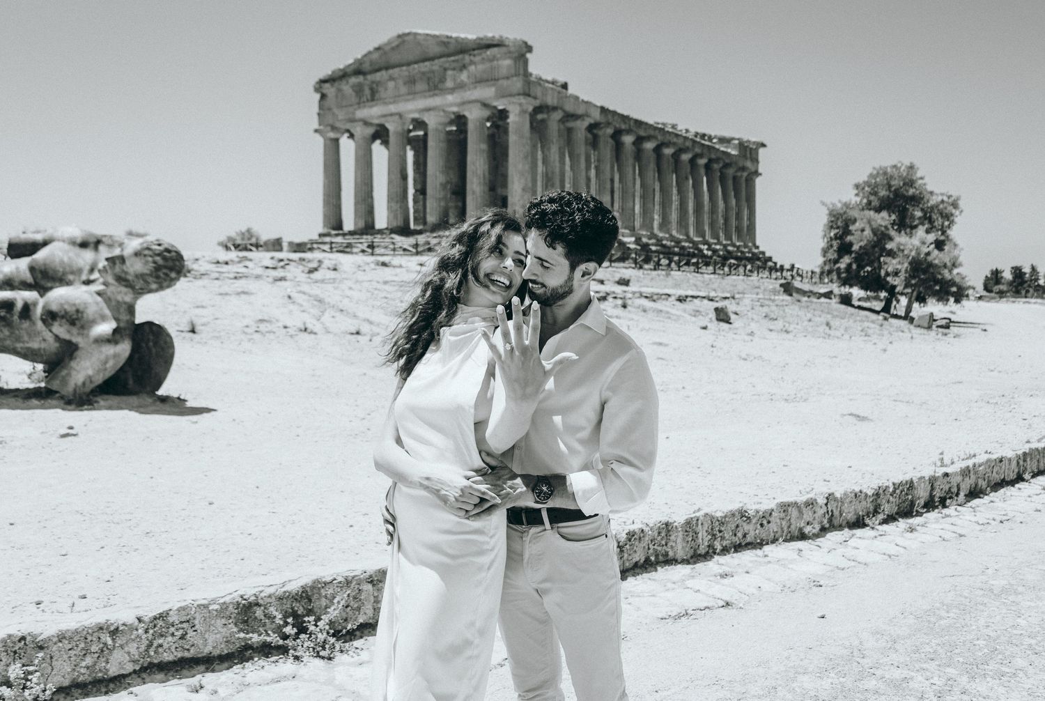 A couple in light colored clothing dances together near ancient temple ruins.