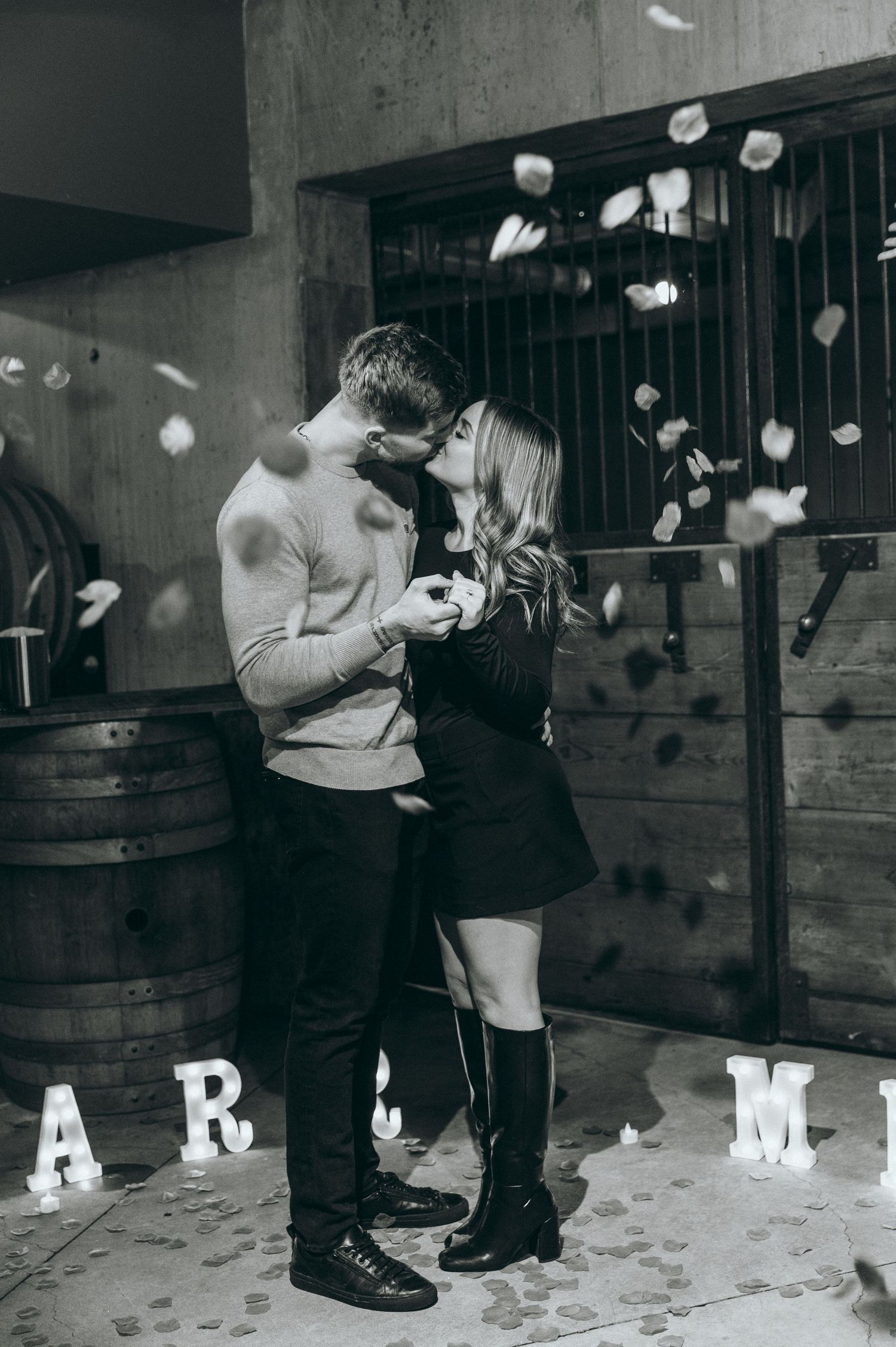 A couple embracing in a wine cellar with falling confetti and letter decorations.