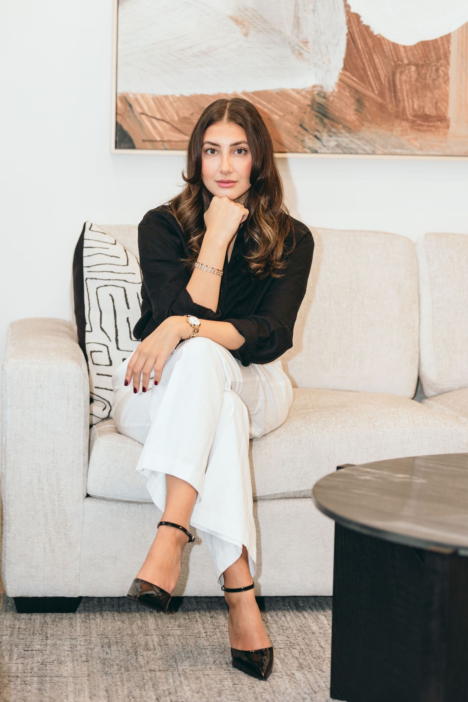 Professional portrait of a woman in business attire sitting confidently on a beige couch.