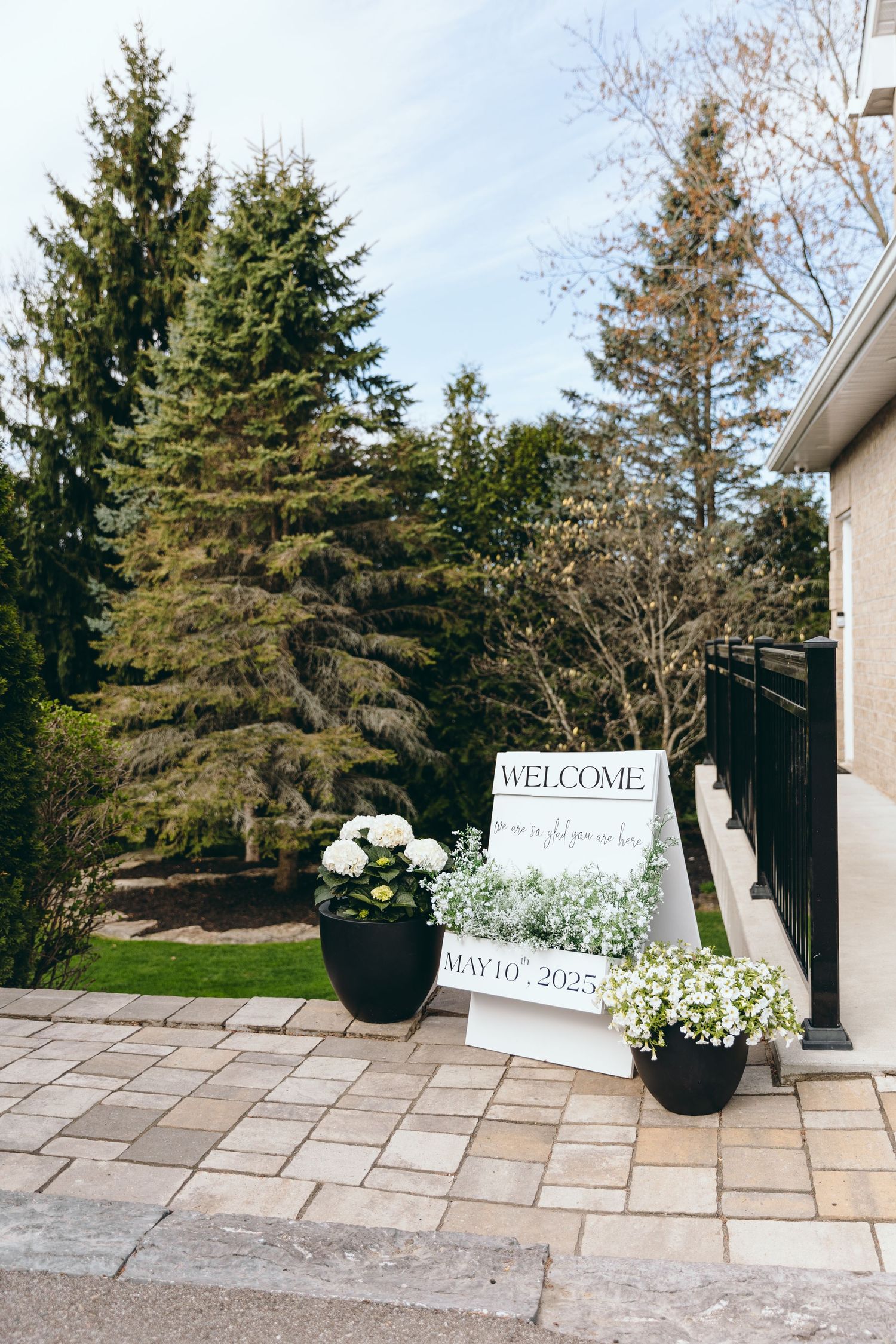 Outdoor wedding venue entrance with welcome sign and potted floral arrangements.
