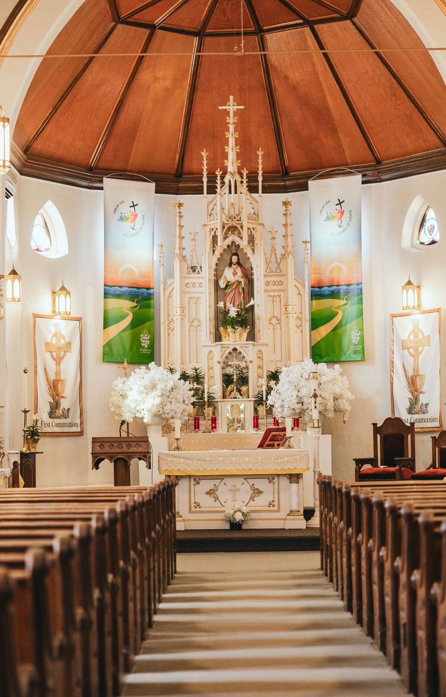 Interior of a Catholic church with ornate altar, wooden pews, and white floral decorations.