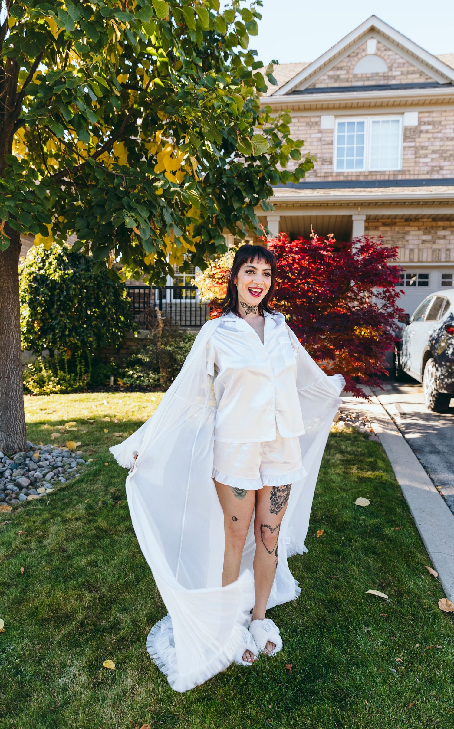 White wedding dress flowing in the breeze against a brick house and autumn foliage.