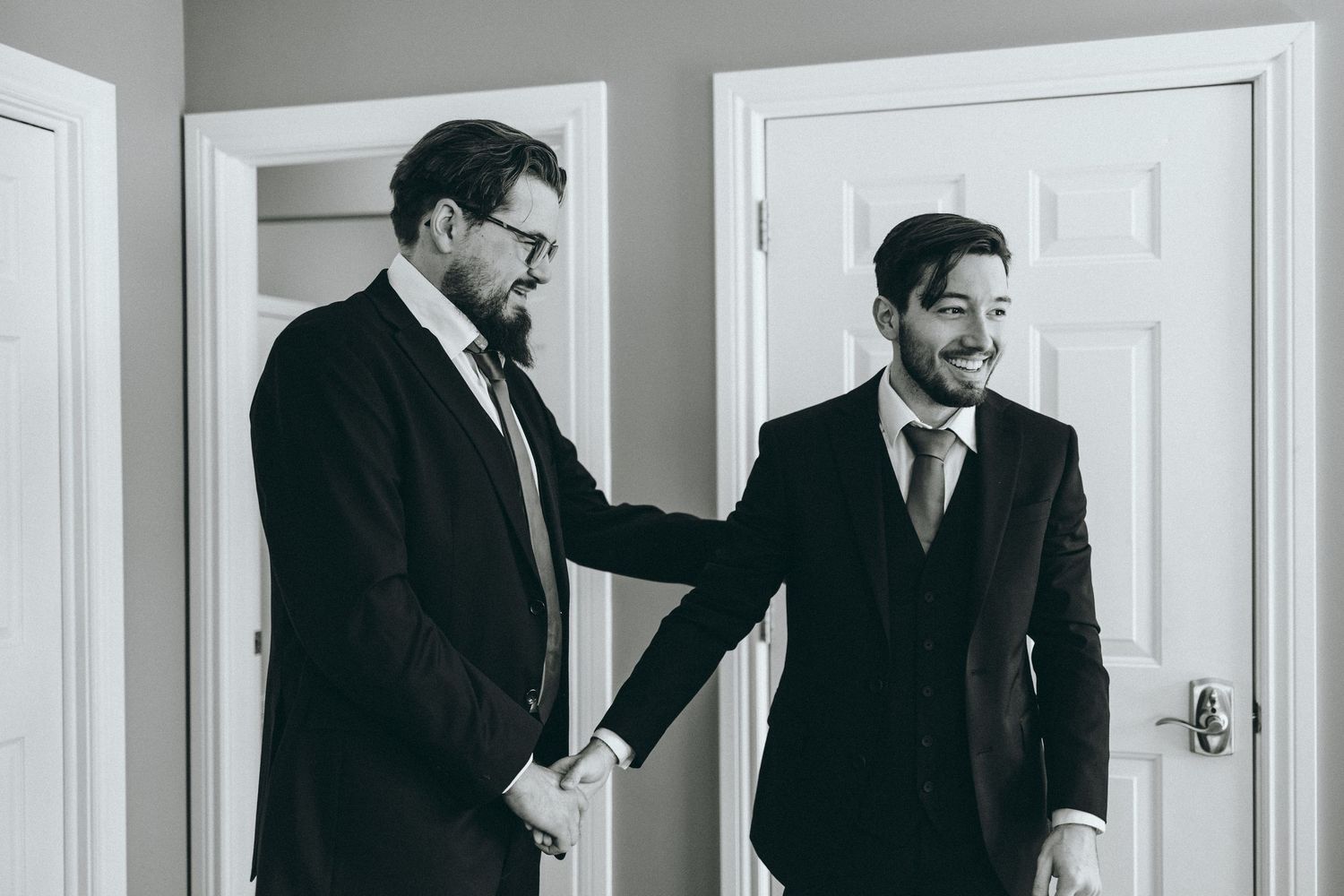 Groomsmen in black suits sharing drinks and conversation in a bright indoor setting.