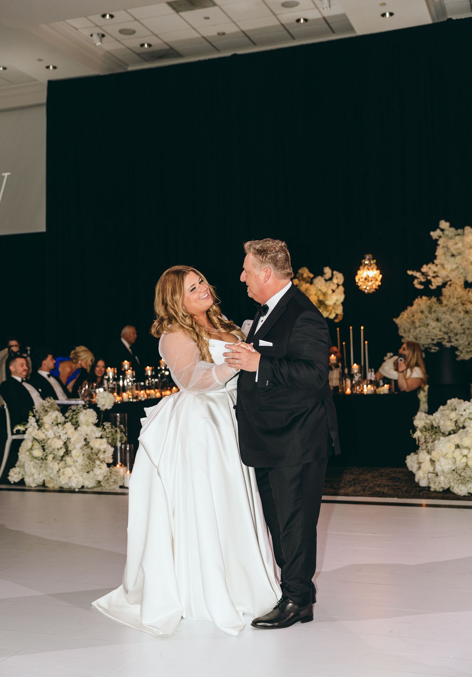 Couple shares intimate dance moment on white dance floor at wedding reception.