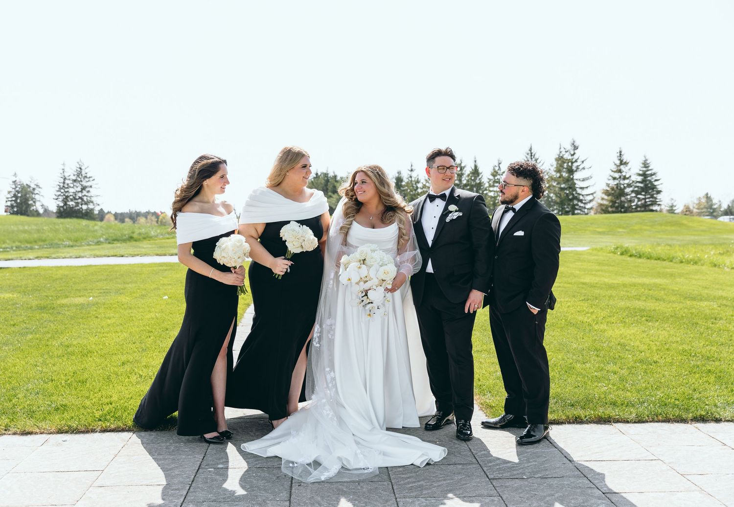 Wedding party in black and white attire poses together on outdoor stone patio.