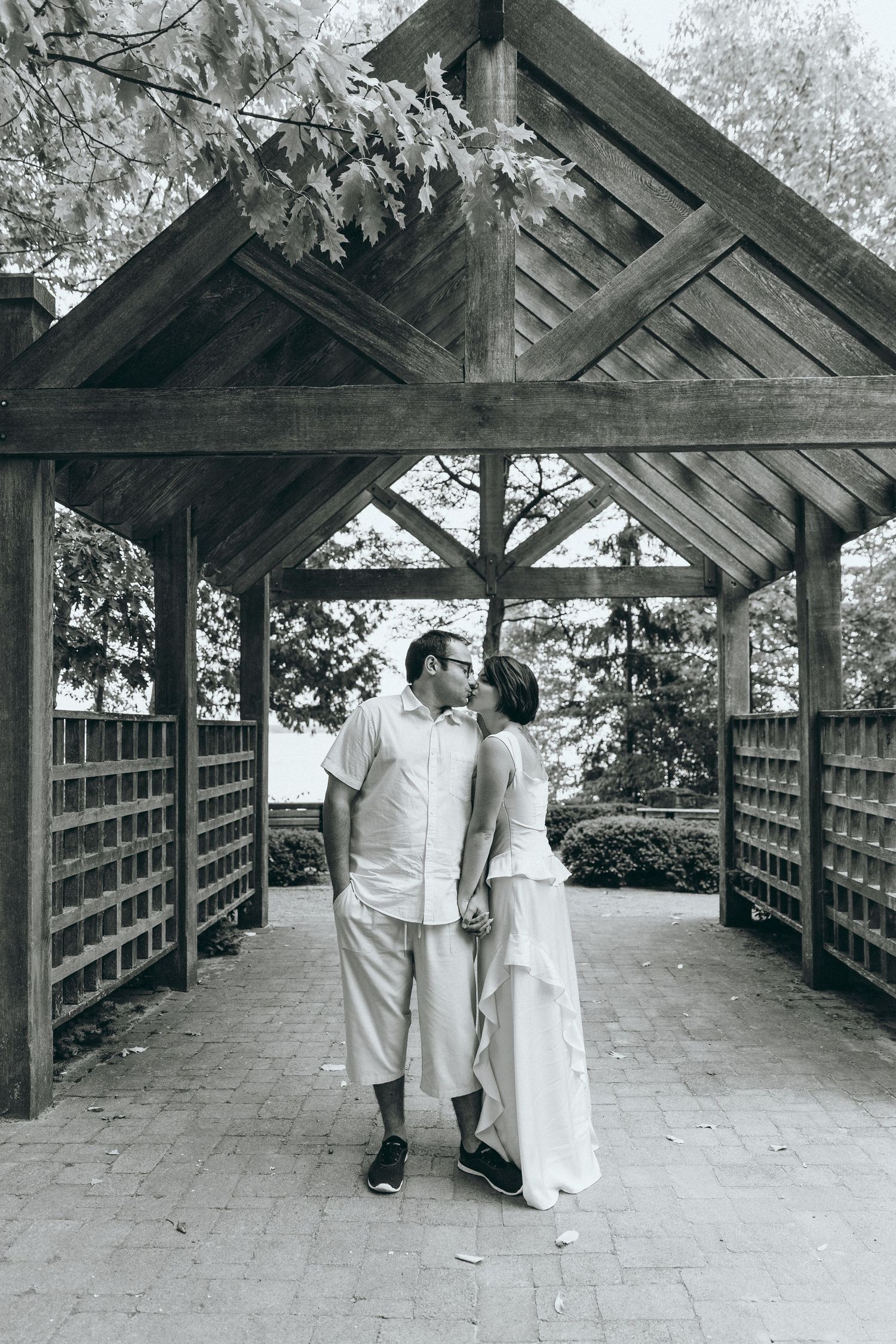 A couple in white attire walking along a covered wooden walkway in a romantic setting.