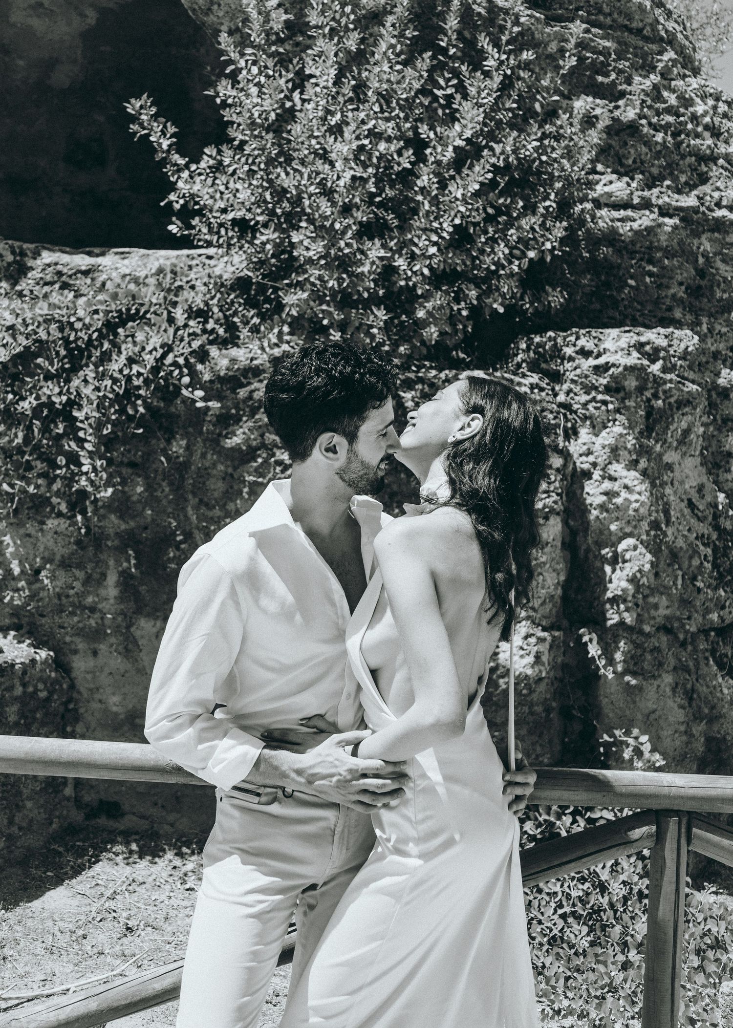 Intimate outdoor portrait session with couple in white clothing near wooden railing.