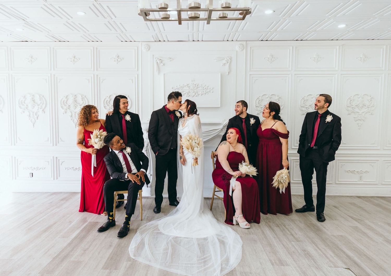 Wedding party poses against white walls in burgundy and black formal attire.
