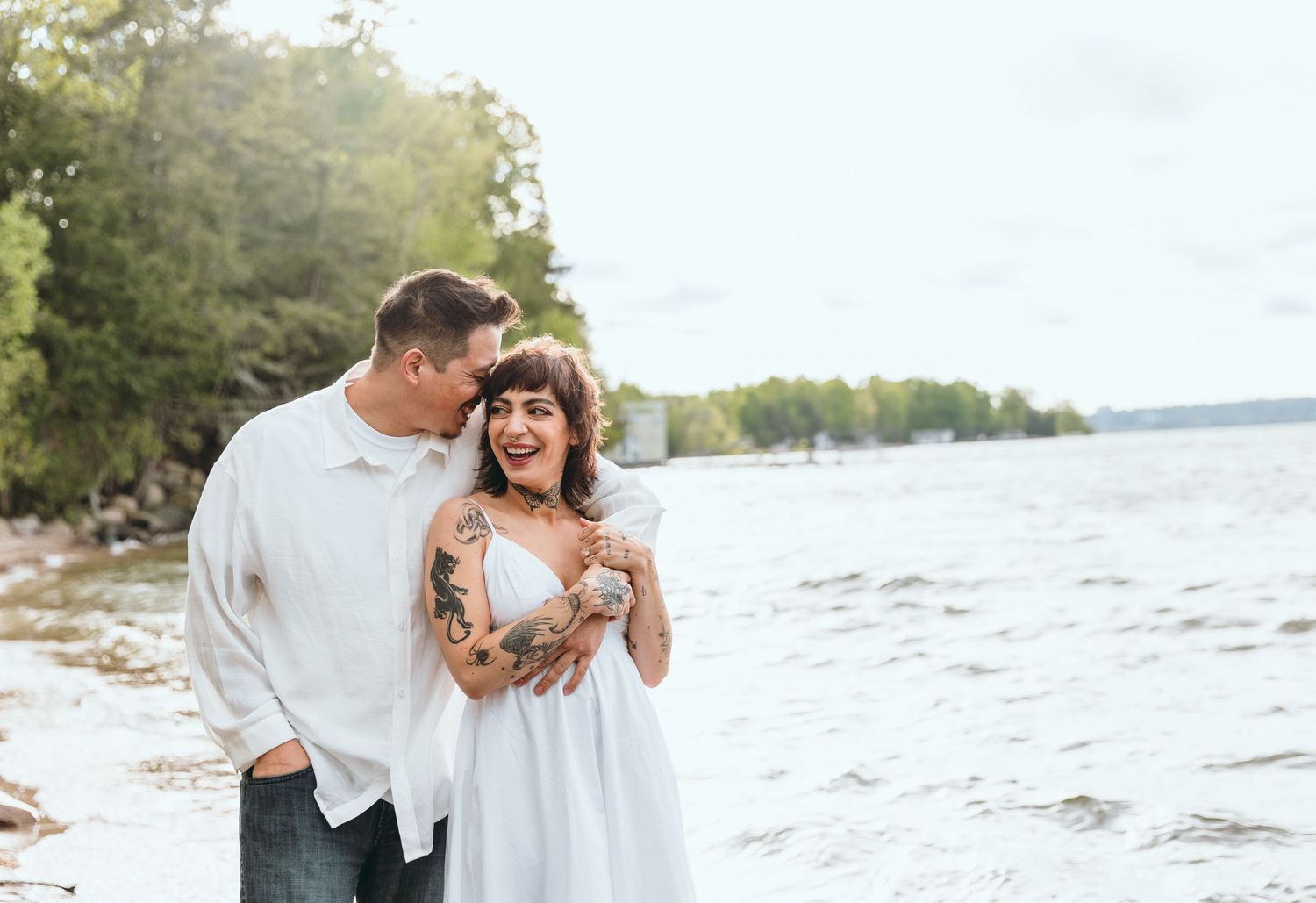 Couple sharing romantic moments along lakeside beach at golden hour.