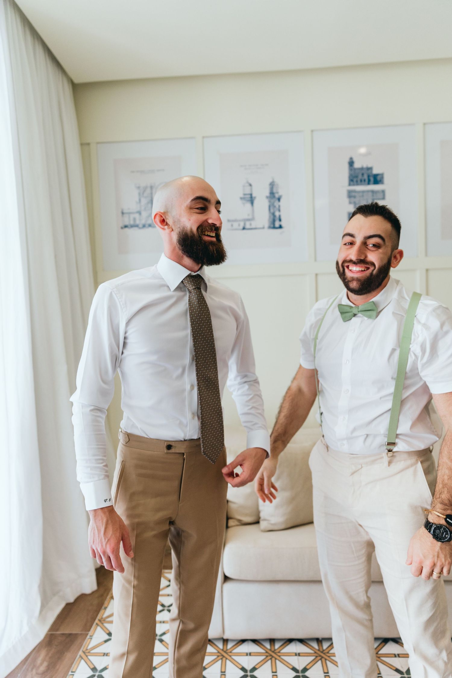 Groomsmen in white shirts and tan vests share laughs and candid moments in a bright room with framed artwork.
