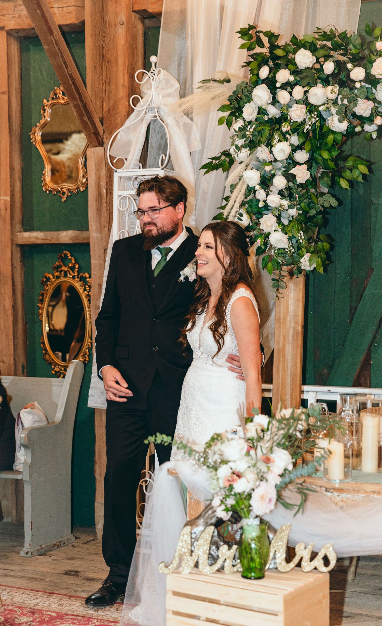 Wedding celebration in barn venue decorated with white floral arrangements and elegant draping.