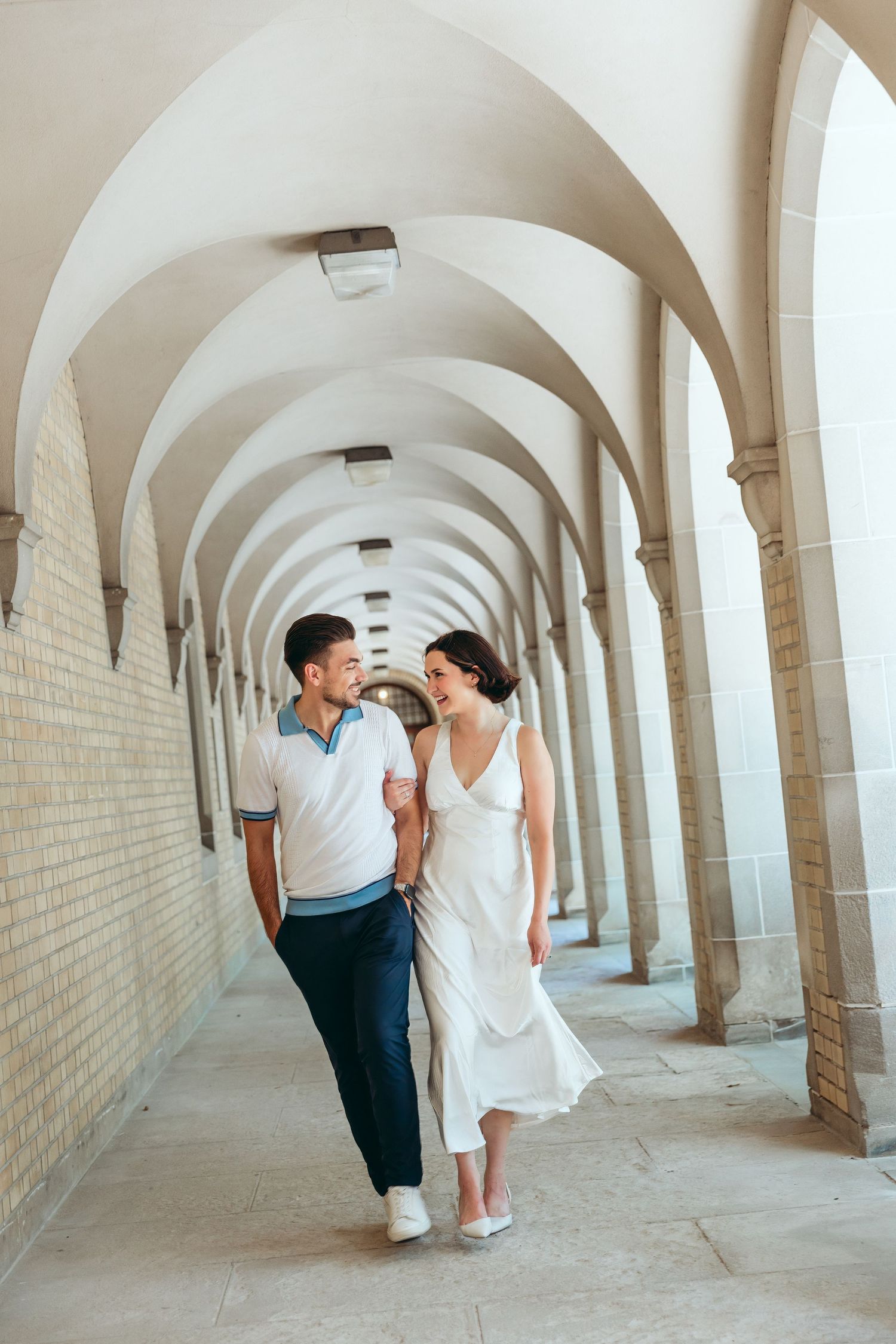 Couple walking through arched colonnade hallway with repeating architectural elements.