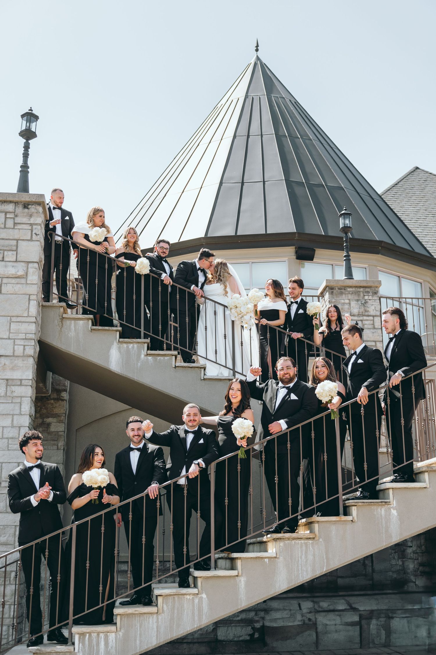 Wedding party arranged on outdoor staircase with conical tower in background.