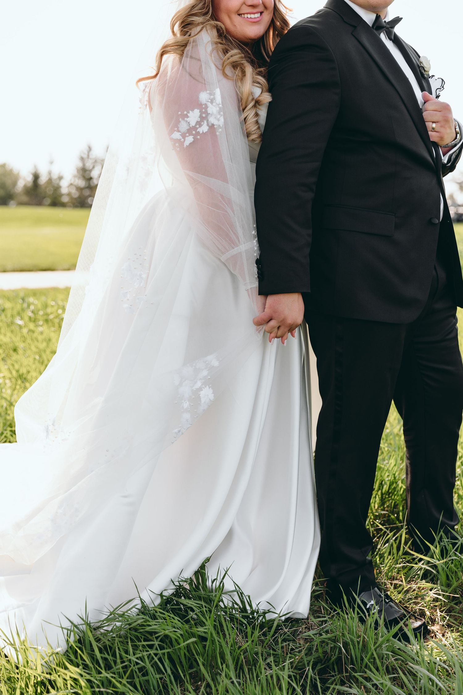 A wedding couple stands together in tall grass during their outdoor celebration.