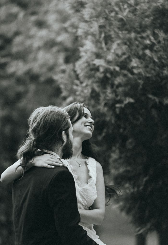 Black and white portrait of wedding couple embracing outdoors with natural backdrop.
