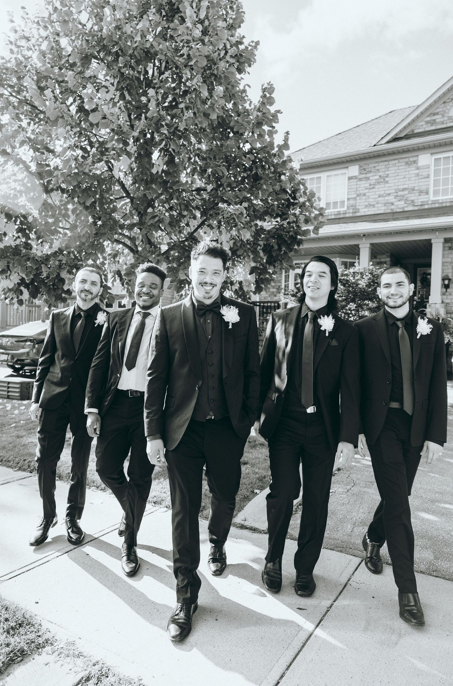 A black and white photo of groomsmen walking together on a sidewalk wearing formal suits.
