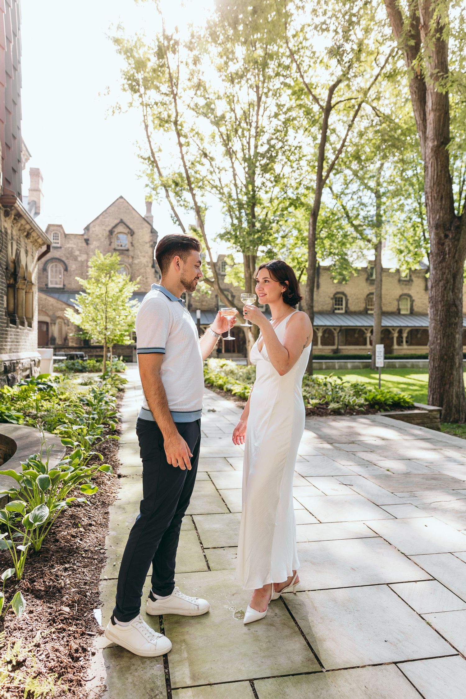 Couple enjoying playful moments on a stone pathway surrounded by trees and buildings.