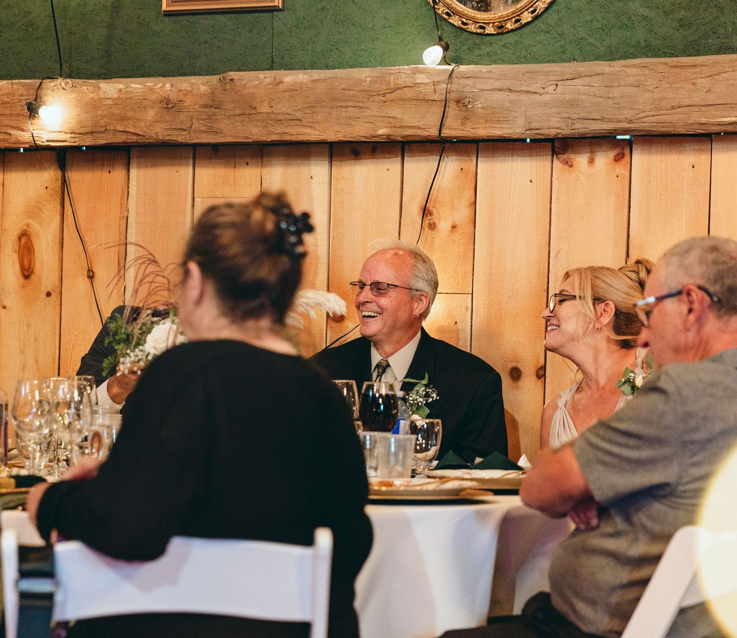 Wedding reception guests seated at tables in rustic barn venue with green walls.