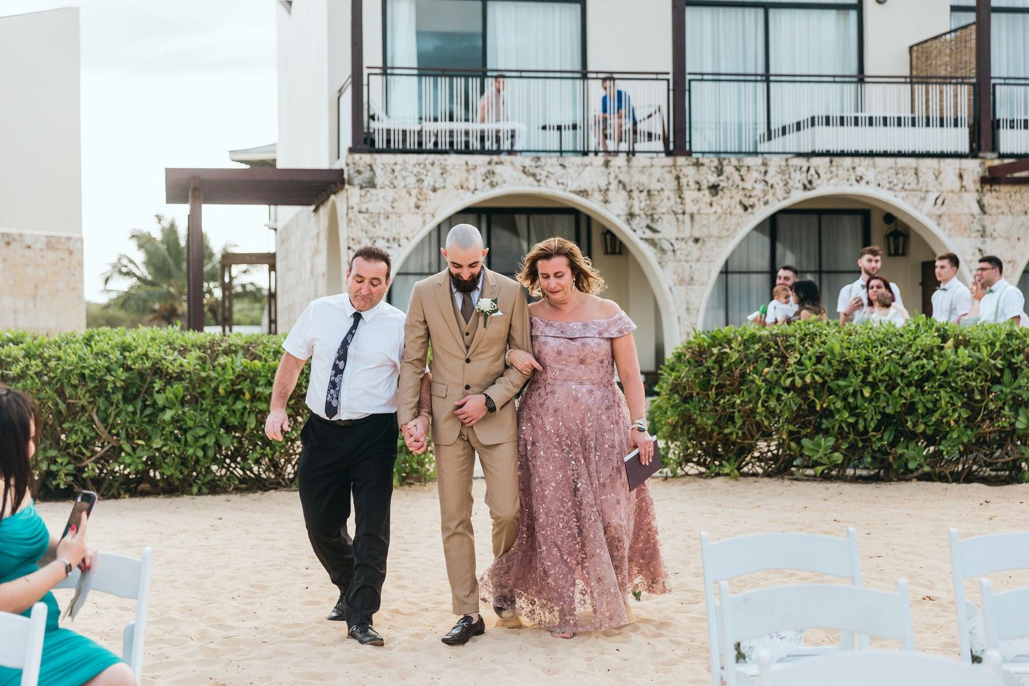 Wedding party members walk along stone pathway outside resort building.