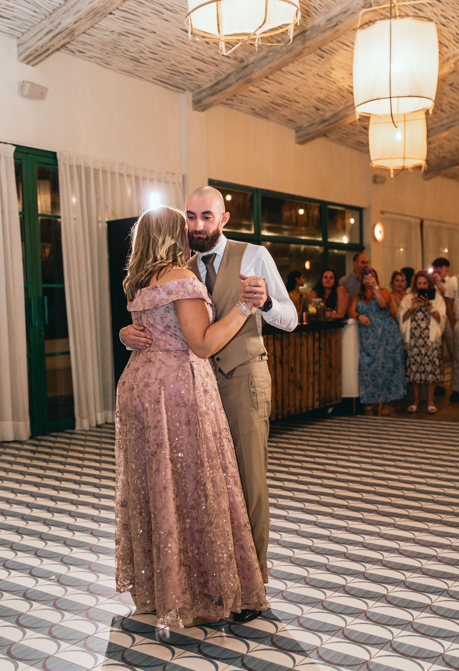 A couple shares an intimate dance in formal attire on a geometric patterned floor under pendant lights.