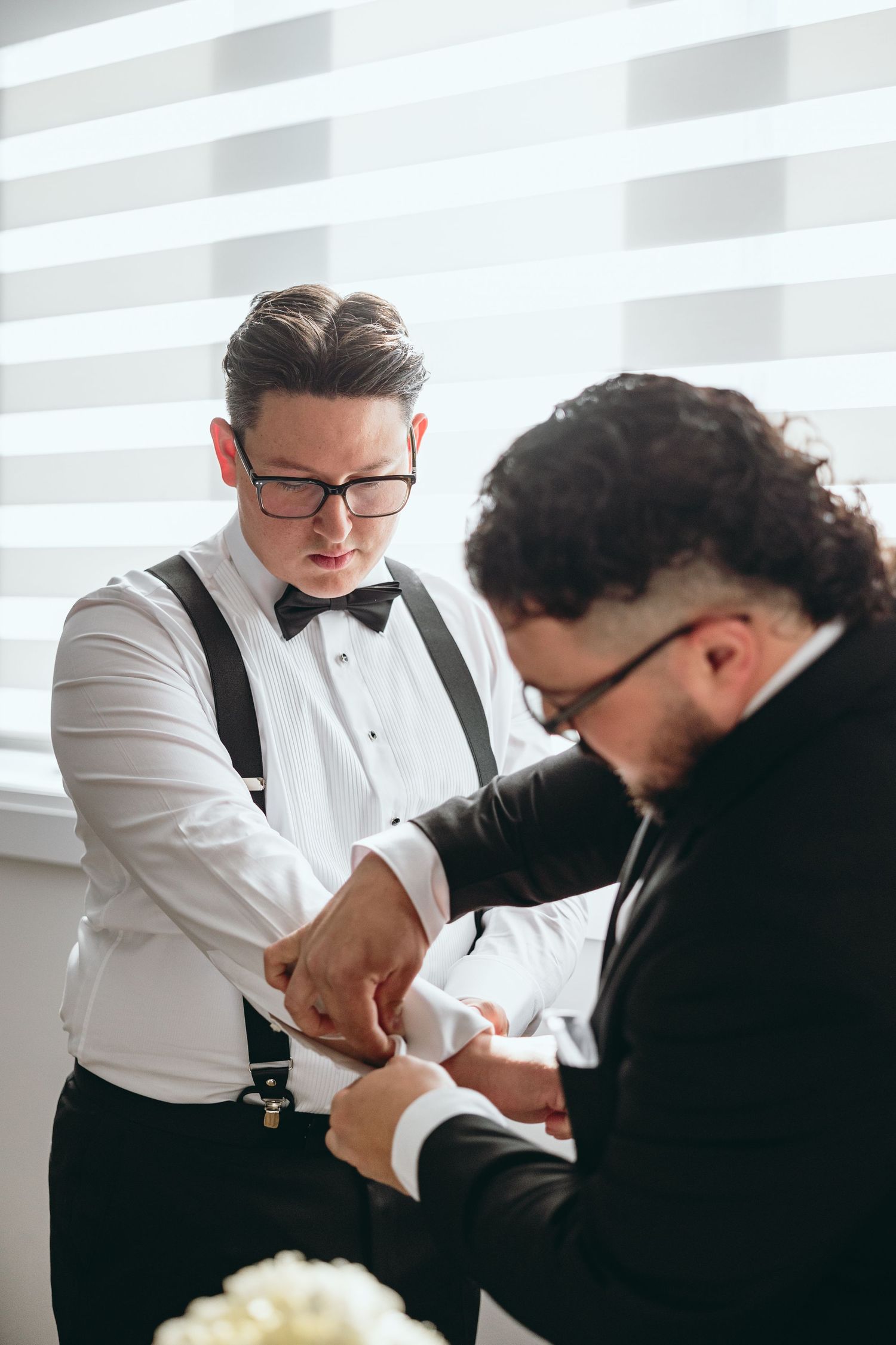 Two people in formal attire having a candid moment during wedding preparations.