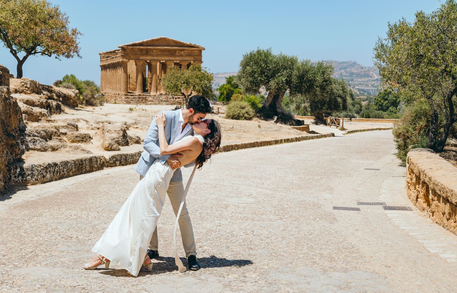 A scenic view of an ancient Greek temple surrounded by olive trees and pathways.
