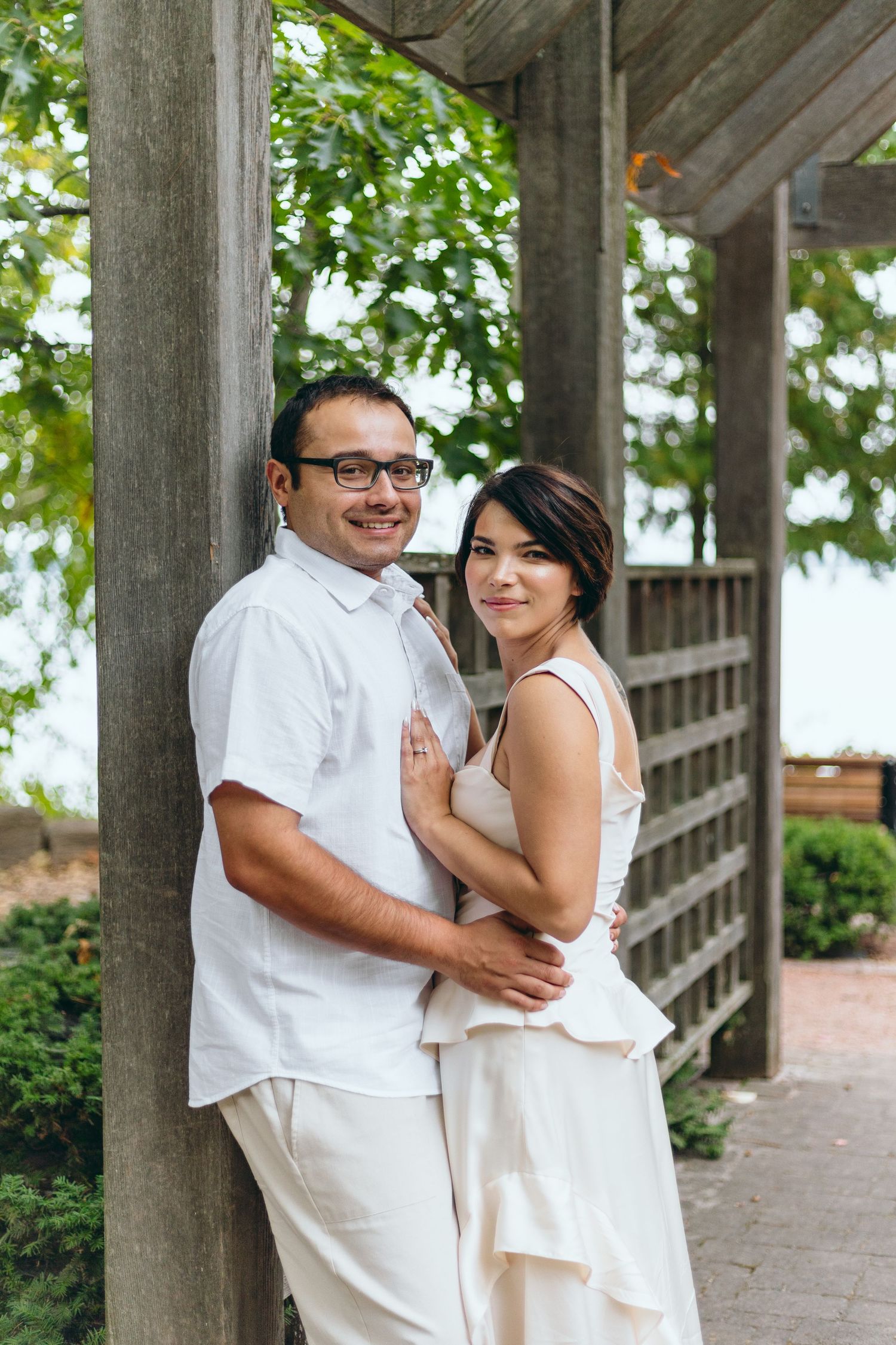 A happy couple in matching white outfits posing together under a covered walkway.