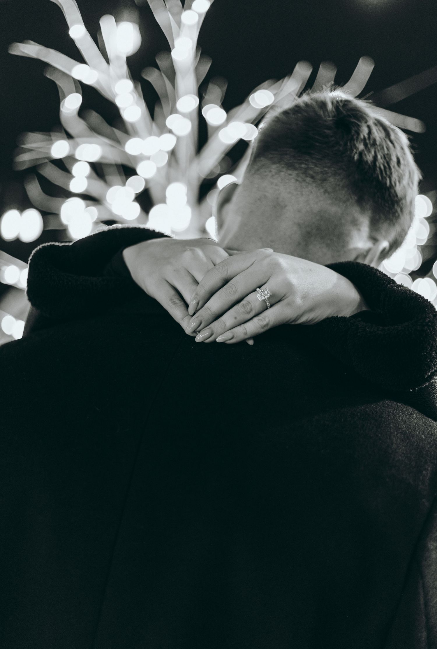 Black and white silhouette of couple embracing with bokeh lights behind them.