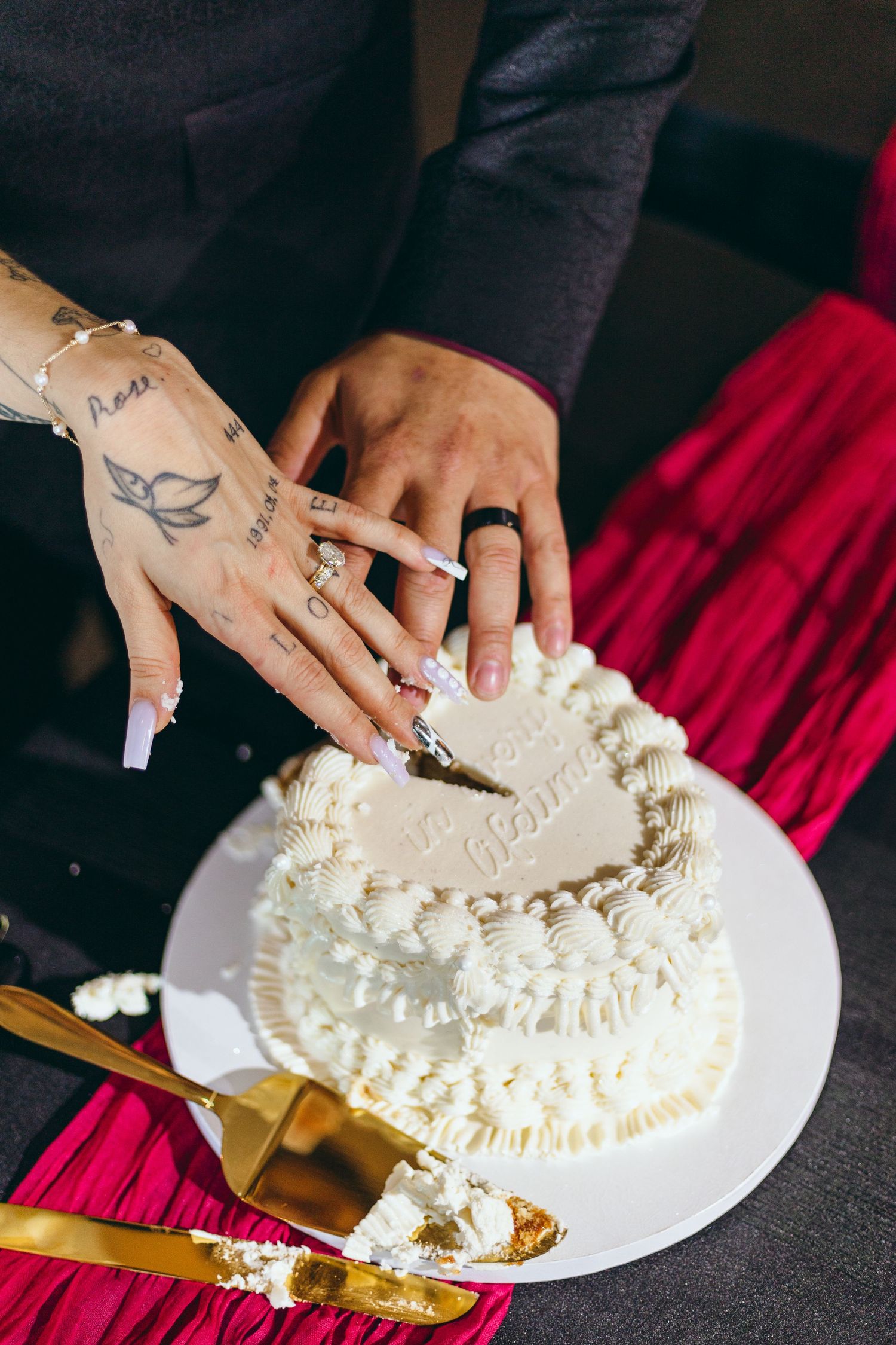 Close-up of hands with tattoos cutting into an elegant white wedding cake.