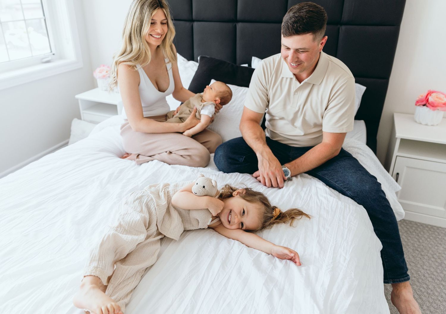 A family sharing a relaxed moment together on a bed with white linens and black headboard.