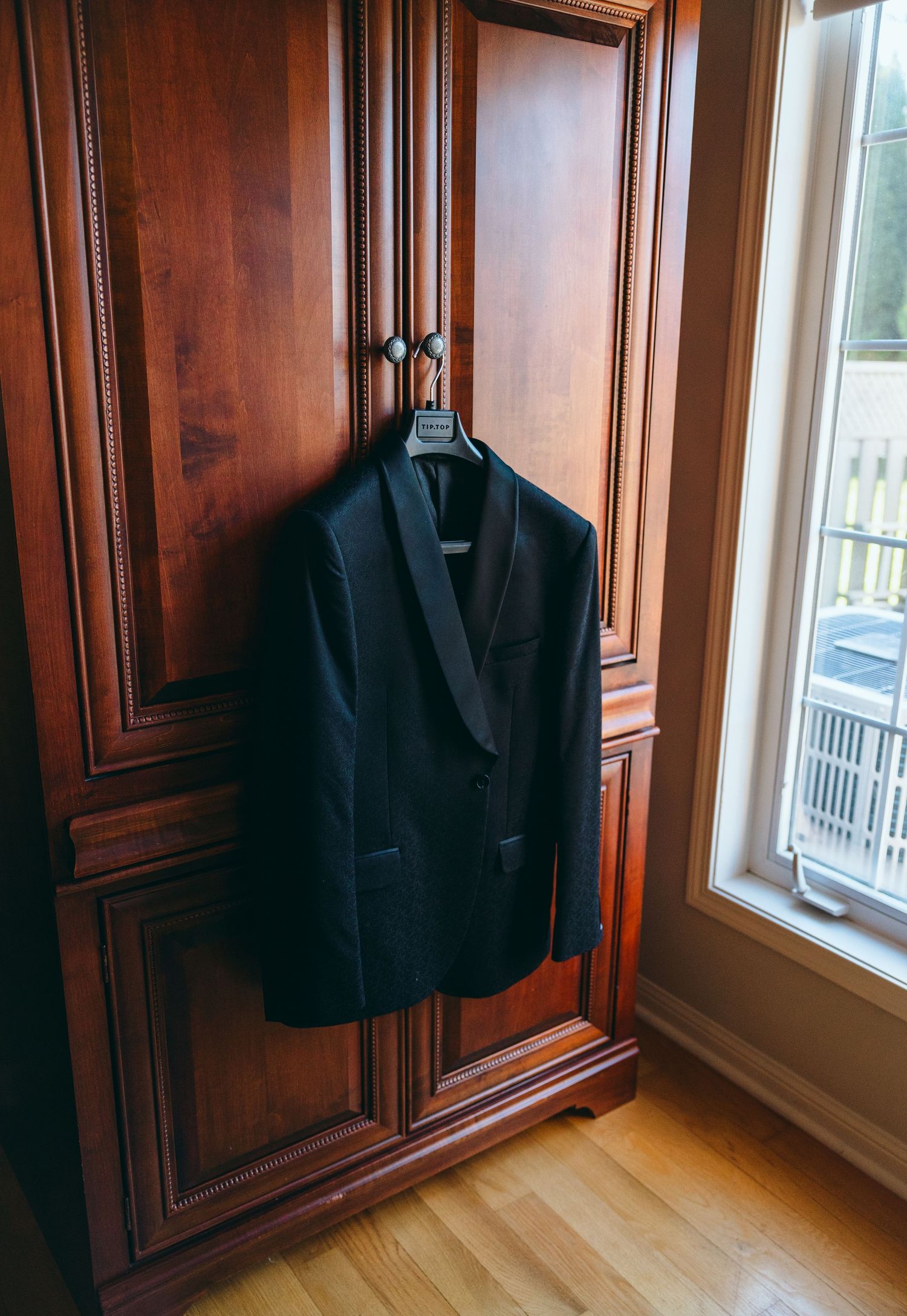 Dark suit jacket hanging in a wooden wardrobe near a window.