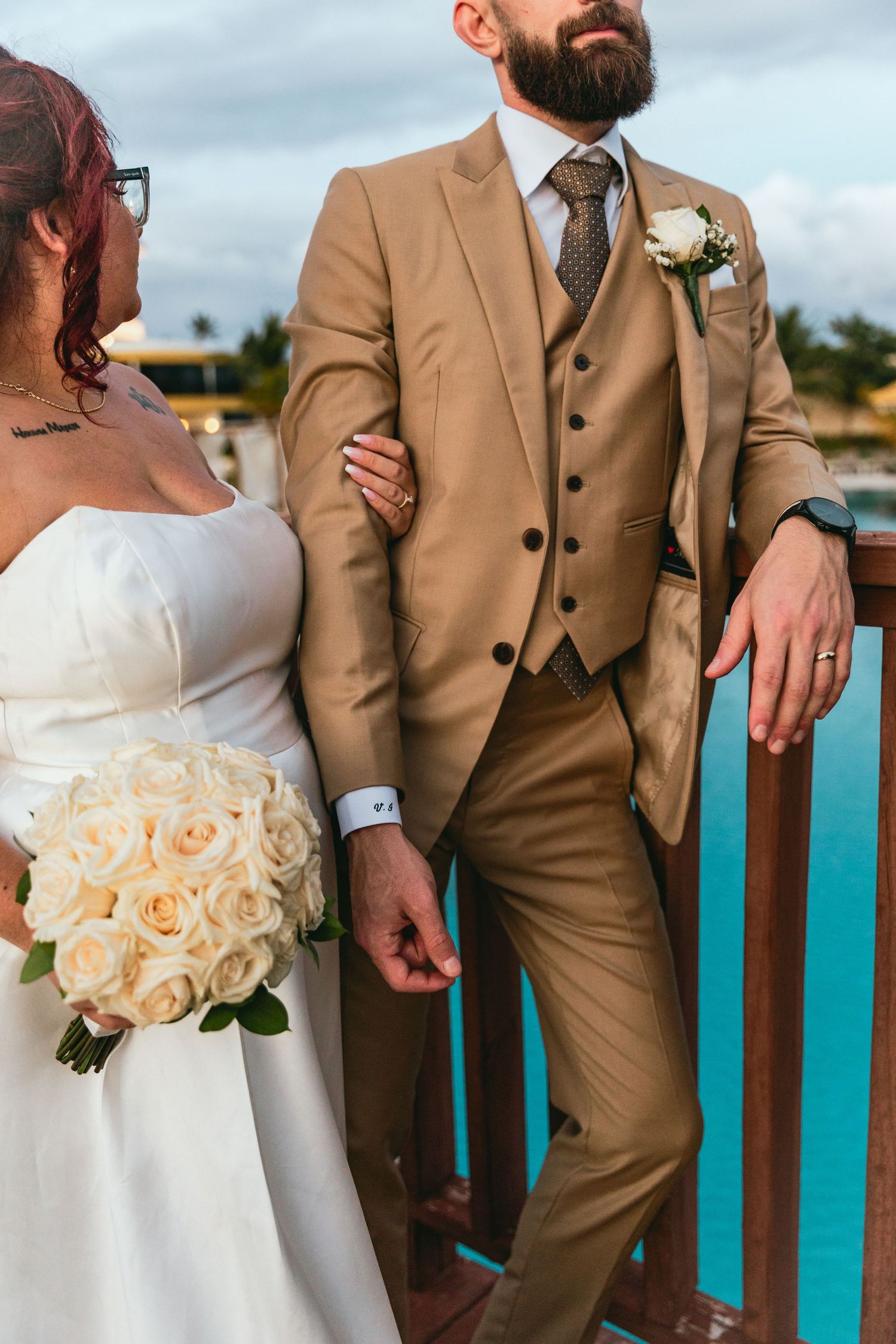 Wedding details showing a tan three-piece suit and white rose bouquet against turquoise waters.