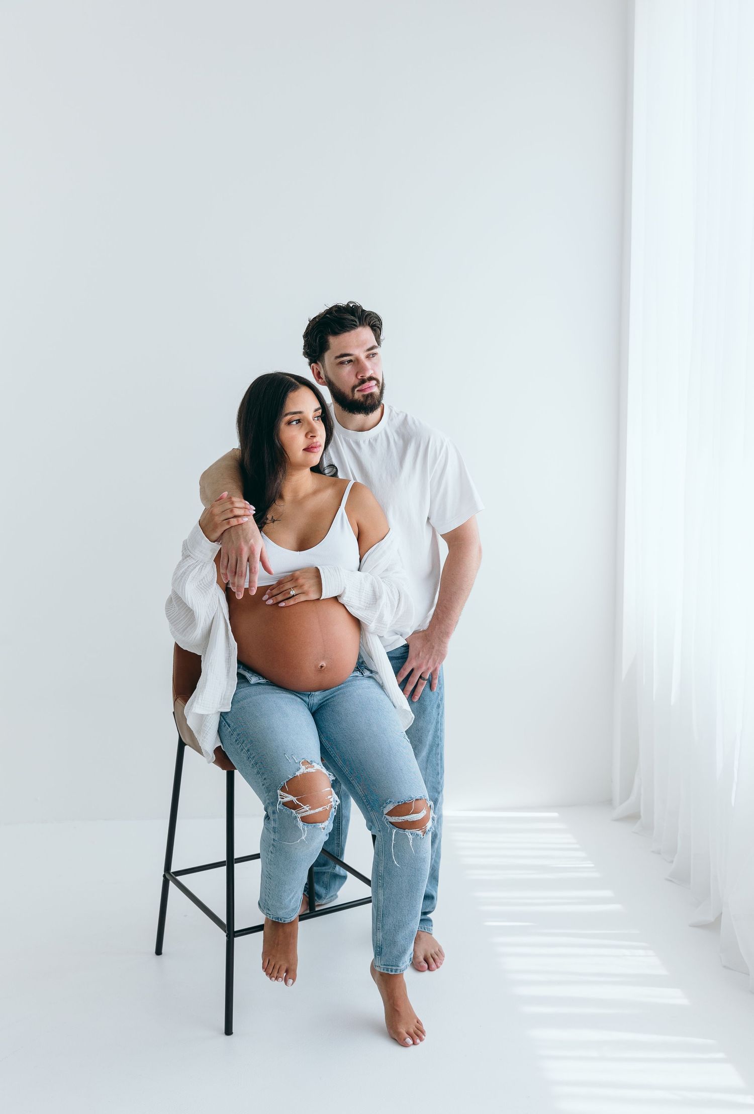 A maternity photoshoot in a minimalist white studio with casual styling.