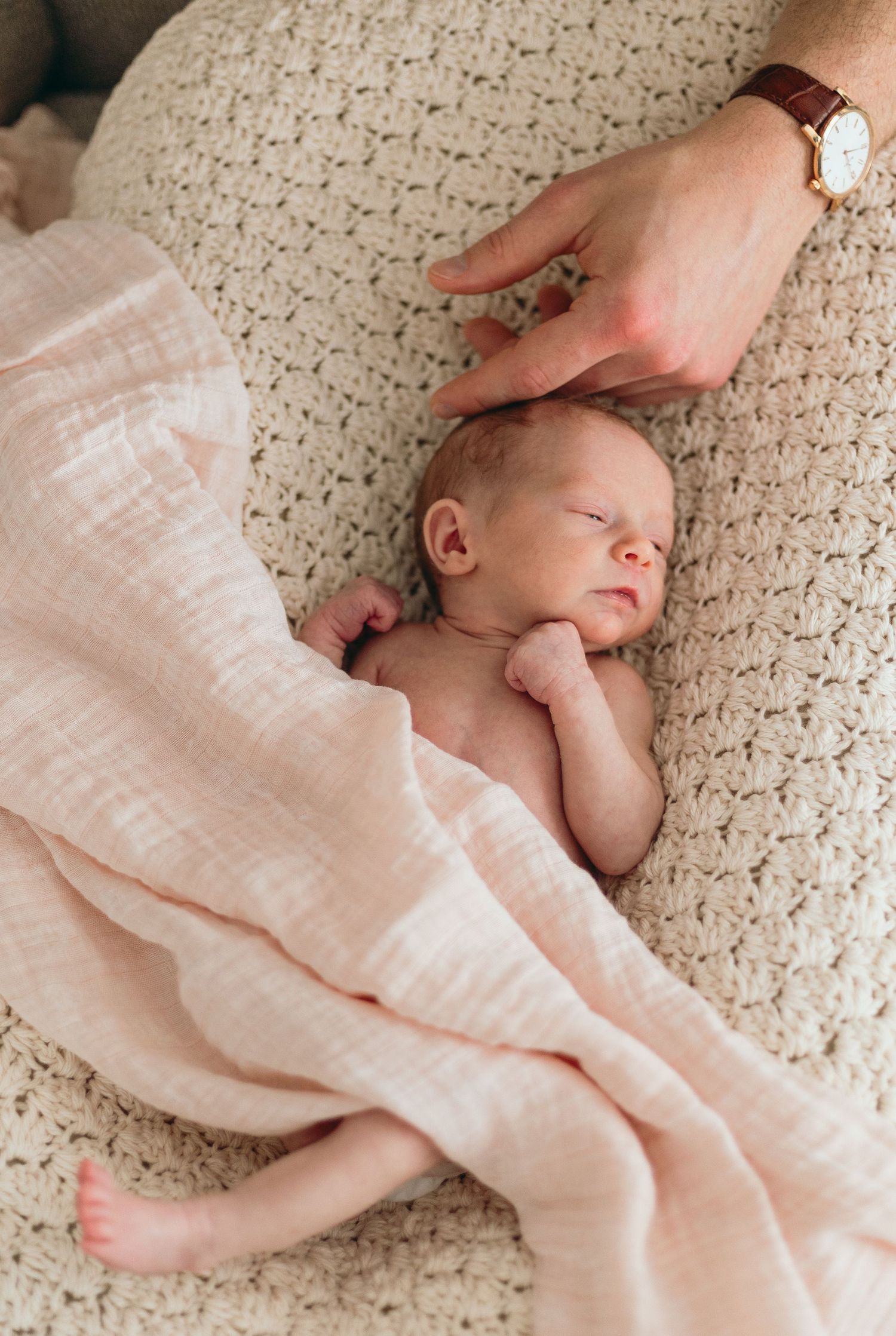 Gentle hands wrapping a newborn baby in soft white blanket on textured surface.