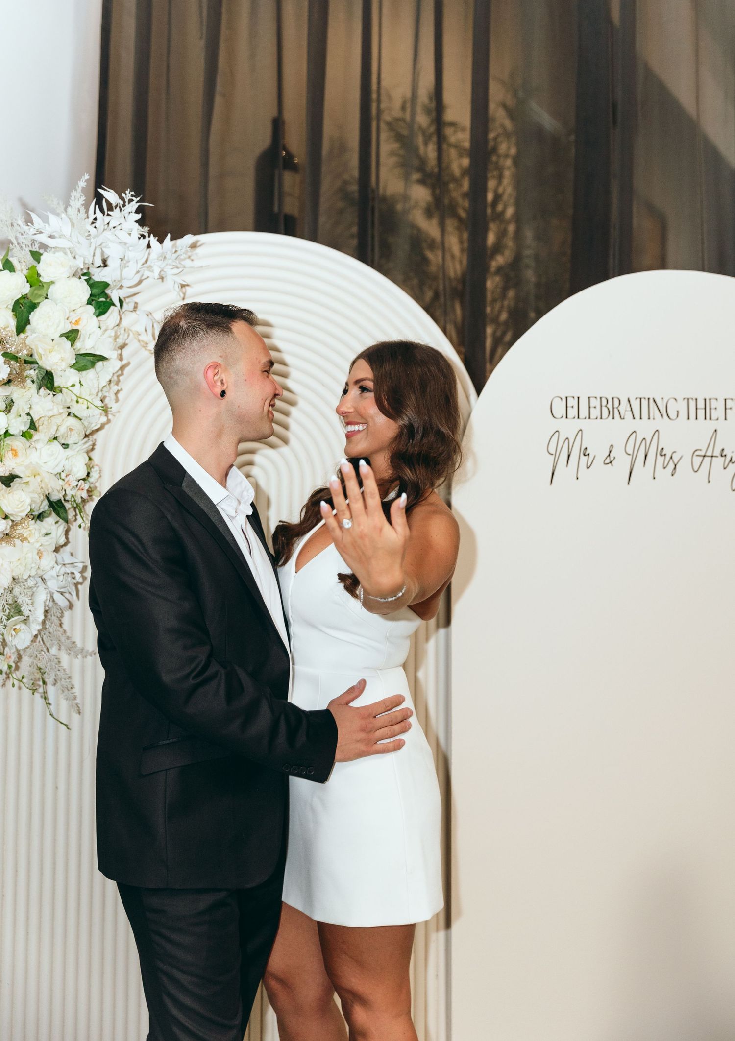 Elegant white curved backdrop with floral arrangements for wedding photos.