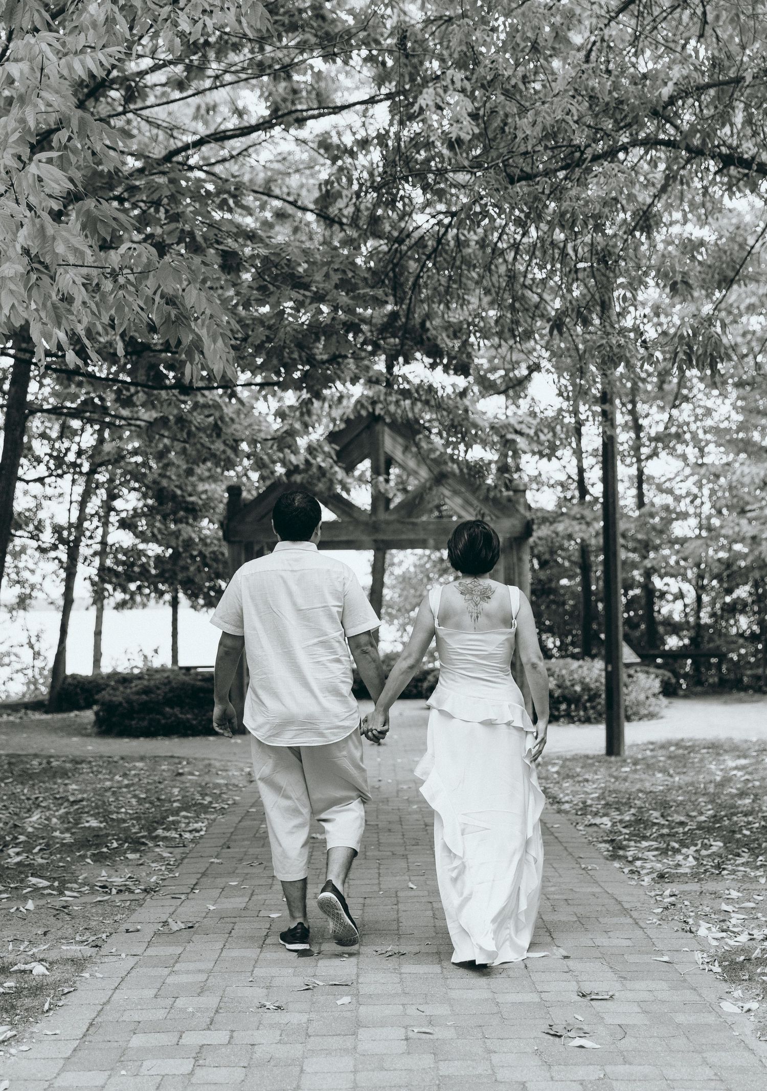 Two people strolling together on a tree-lined path wearing matching white outfits.