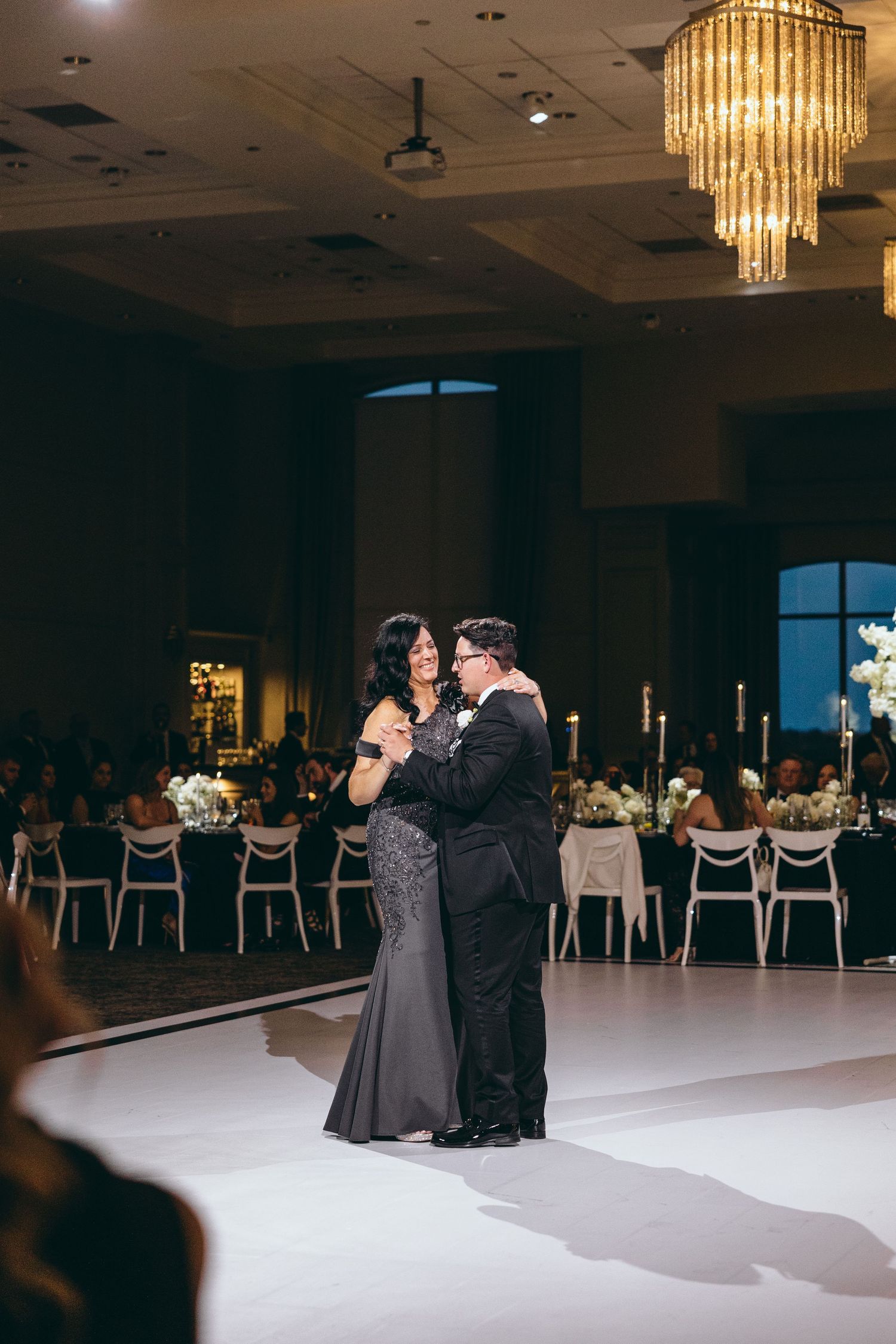 Wedding reception dance floor scene with crystal chandeliers and elegant decor.