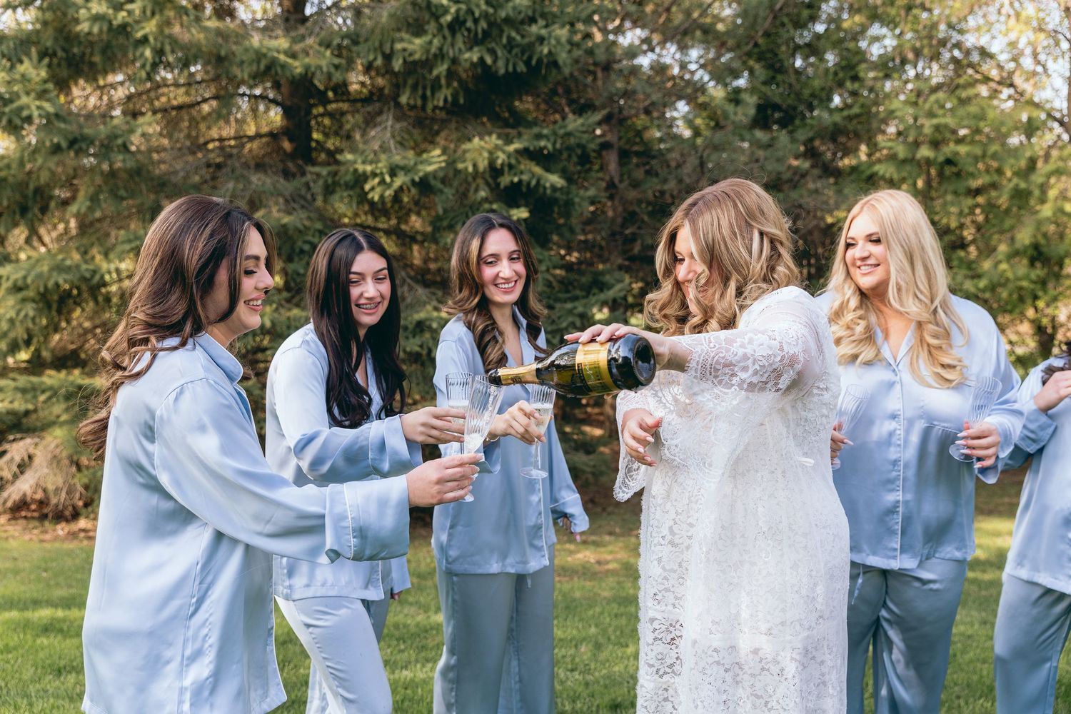 Bridesmaids in light blue denim jackets celebrating outdoors in a garden setting.