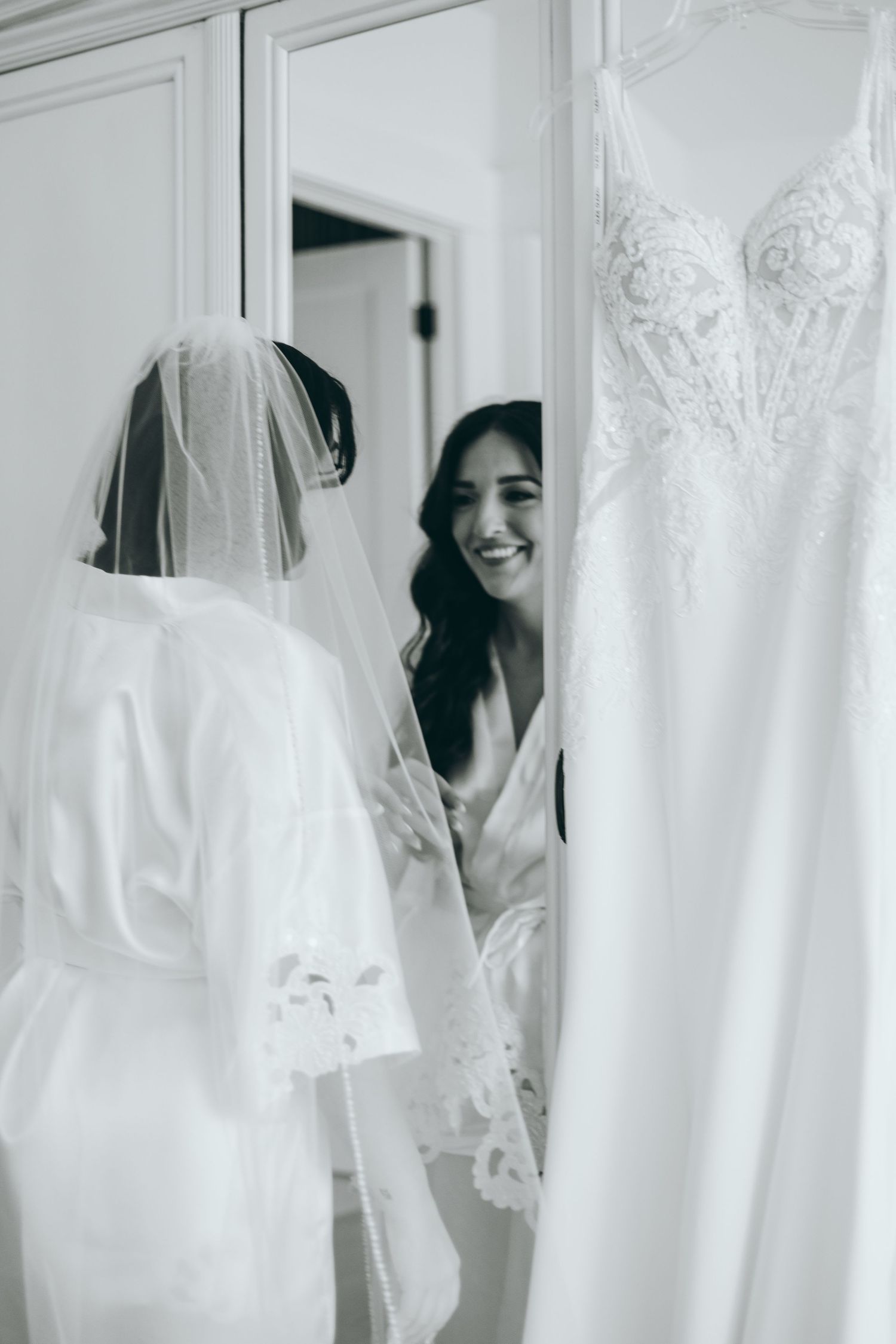 White wedding dresses and robes hanging in a bright room during wedding preparations.