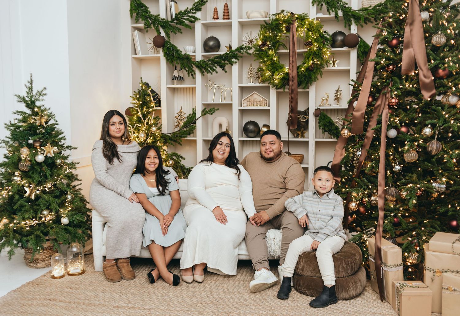 Family of five poses for a festive Christmas photo surrounded by decorated trees and holiday shelving.
