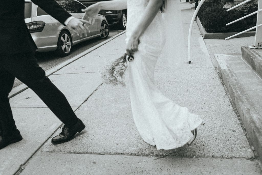 Wedding couple's feet and dress hem shown while walking on sidewalk.