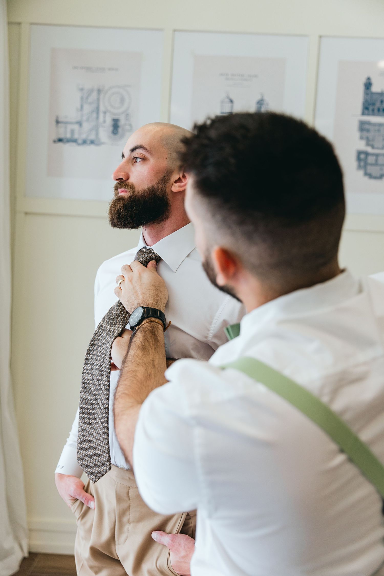 Two people in formal attire getting ready in a room with framed artwork.