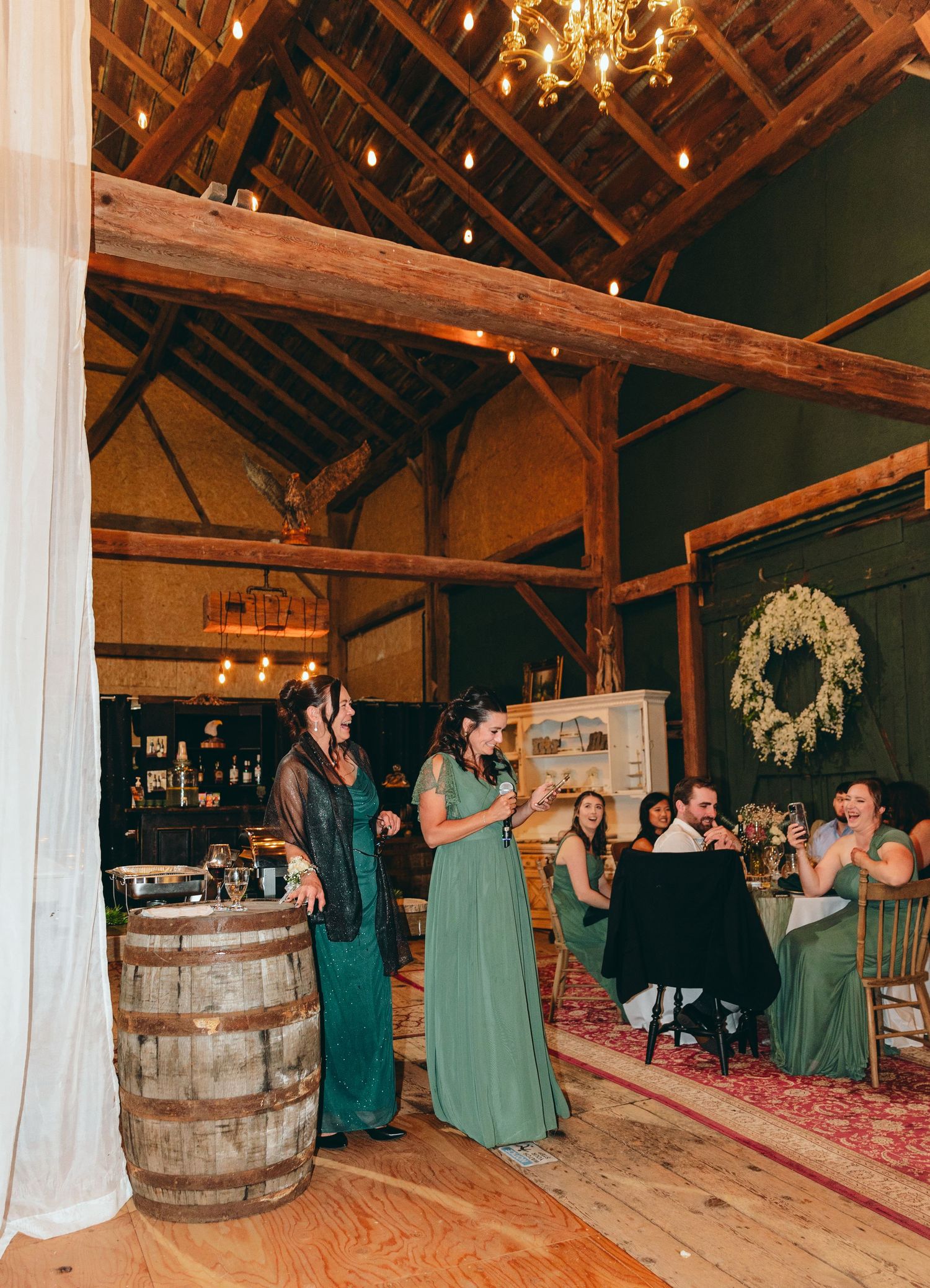 Wide view of rustic barn wedding reception with wooden barrels and guests dancing.