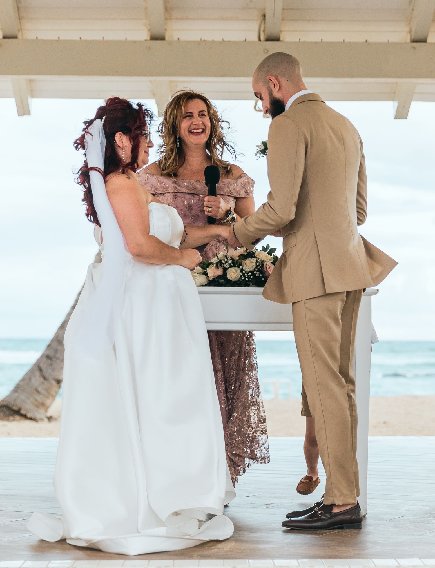 A wedding celebration unfolds in a coastal gazebo with ocean waves visible in the background.