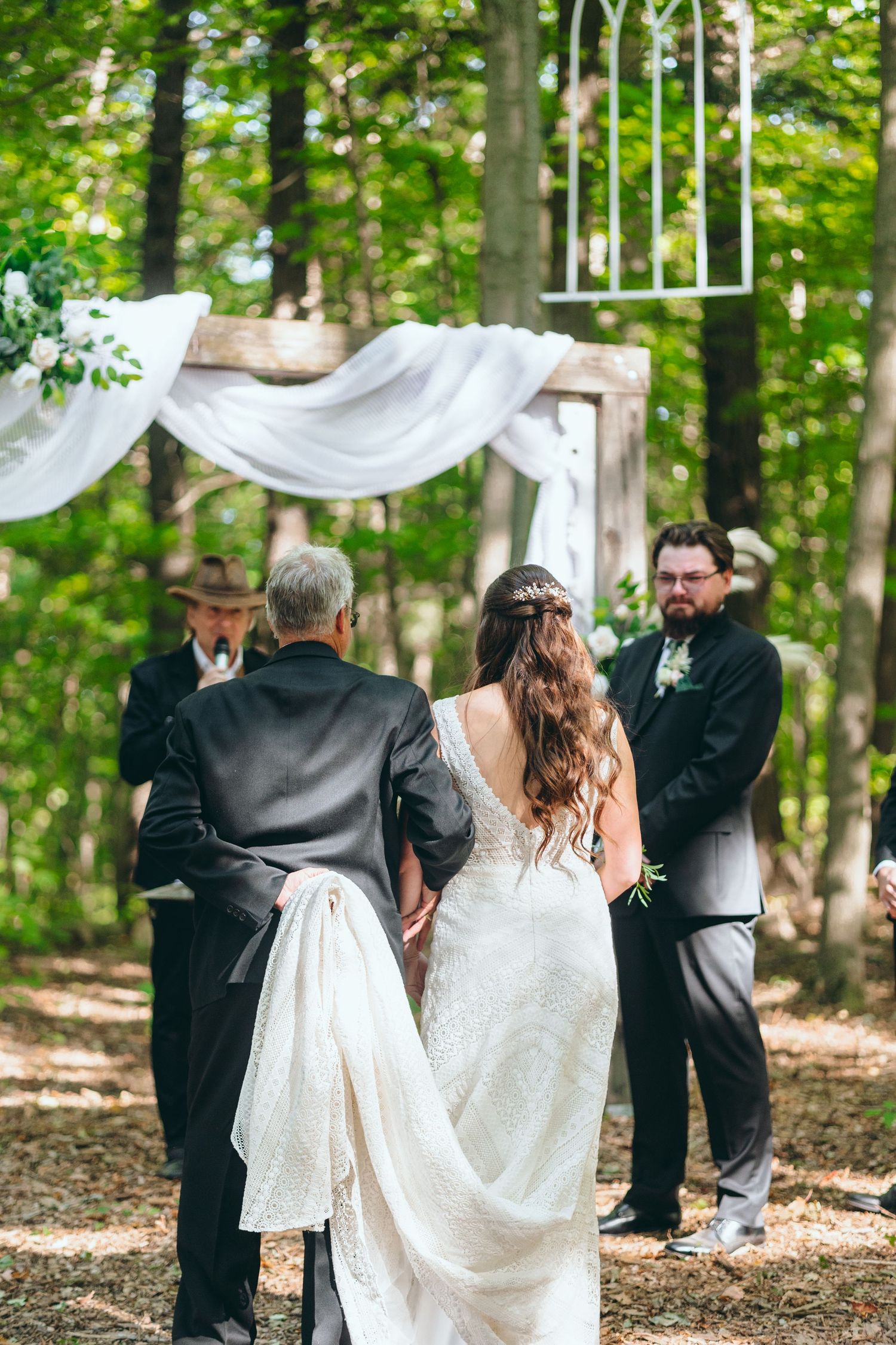 Wedding party members dance and celebrate in a forest setting with white decorative elements.
