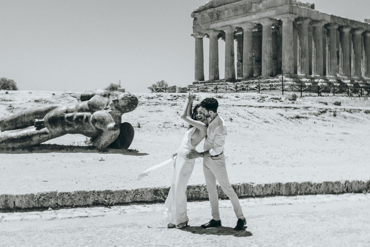 Black and white photo of couple embracing near ancient Greek temple columns.
